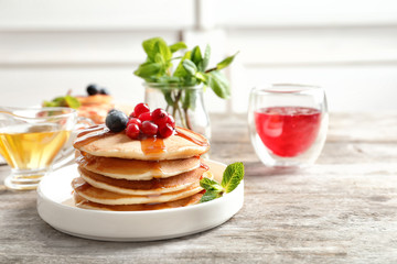 Stack of tasty pancakes with berries and syrup on table