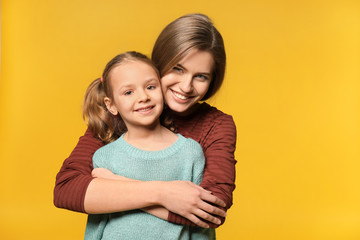 Portrait of mother and cute little daughter on color background