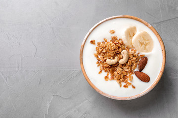 Bowl with yogurt, banana and granola on gray background, top view