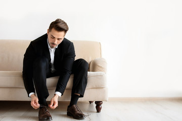 Young man putting on elegant leather shoes indoors