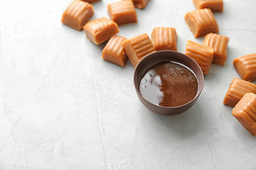 Delicious caramel candies and sauce on light background