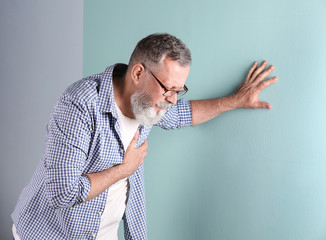 Mature man having heart attack on color background