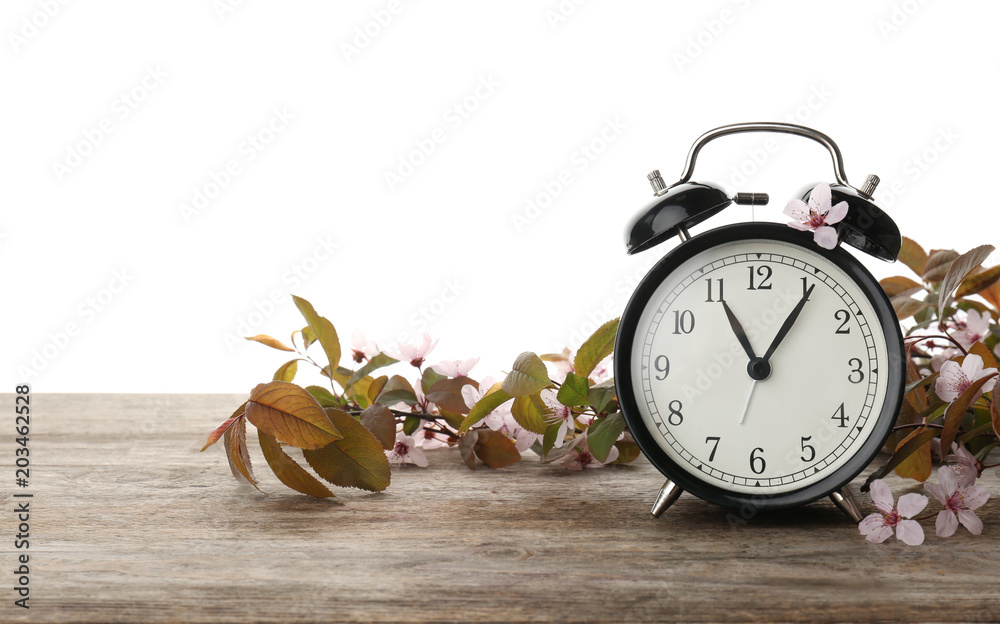 Poster alarm clock and branch with spring blossoms on wooden table against white background. time change co