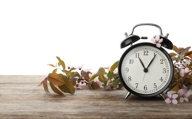 Alarm clock and branch with spring blossoms on wooden table against white background. Time change...