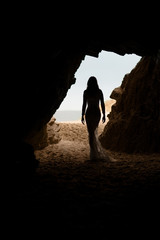 Fototapeta premium Beautiful and sexy woman body silhouette in long dress in a cave