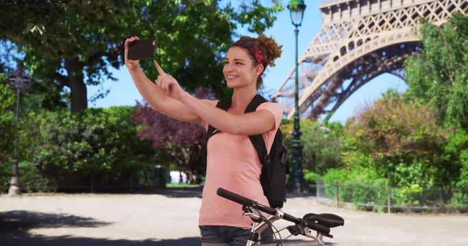 Caucasian brunette on bike ride in Paris stops to take selfie near Eiffel Tower