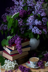 Still life books, coffee and lilacs in the dark key.Spring background