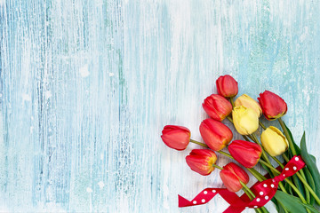 Colorful tulips bouquet decorated with red ribbon on blue wooden background. Top view, copy space. Holiday background.
