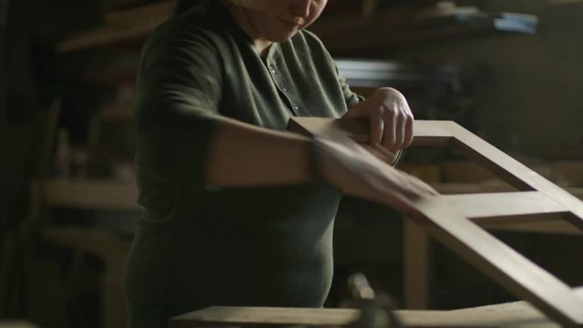 Slow motion tilt up on woman sanding wood frame in workshop / Provo, Utah, United States