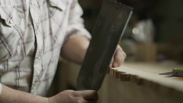 Slow motion tilt down to hands of man detailing edge of wood with saw / Provo, Utah, United States