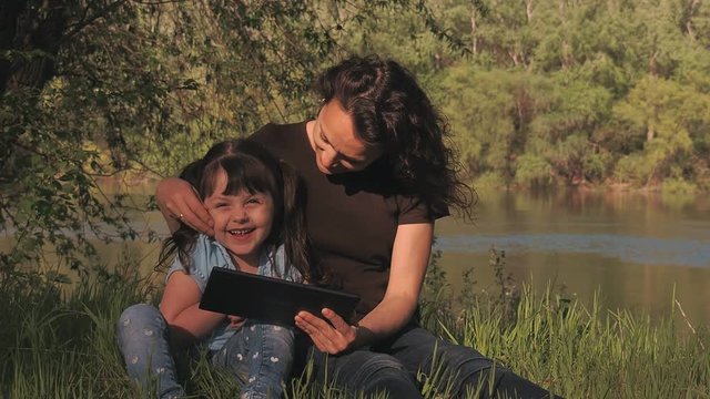 Family in nature with a tablet. A child with her mother on the Internet in nature.