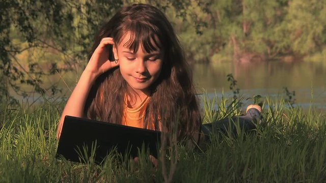 Child on the grass with a tablet. Girl on the Internet in nature.