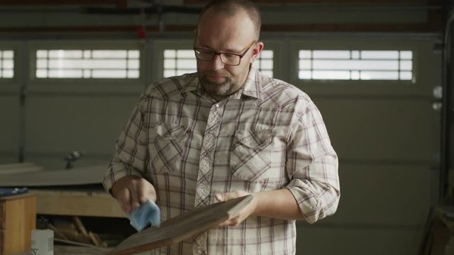 Slow motion zoom in to man cleaning wood plaque in workshop / Provo, Utah, United States