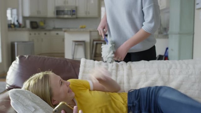 Girl laying on sofa using cell phone then tickled by sister with duster / Highland, Utah, United States