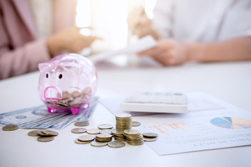 Two couples putting coins into piggy bank, writing to report and using calculator to analysis...
