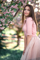 a girl in a pink dress stands smiling near the cherry blossom