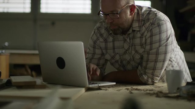 Slow motion tilt up to man using laptop in workshop / Provo, Utah, United States
