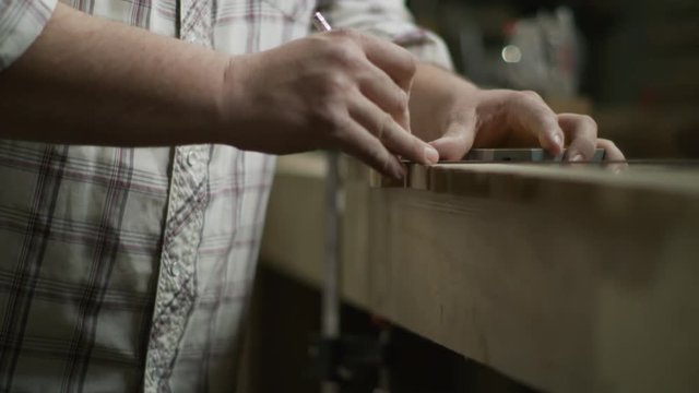 Slow motion tilt up to hands of man marking edge of wood with pencil and ruler / Provo, Utah, United States