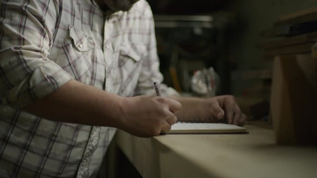 Slow motion tilt up to man writing in notebook with pencil in workshop / Provo, Utah, United States