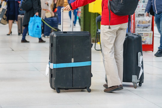 Close-up of young woman hands holding suitcase in modern airport terminal. Travelling guy wearing smart casual style clothes standing with his luggage while waiting for transport