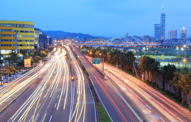 Night scenery of Taipei City, with Taipei 101 Tower in XinYi District, downtown area with arch bridges and car trails on Dike Avenue ~ Romantic cityscape of Taipei at dusk by riverside (long exposure)