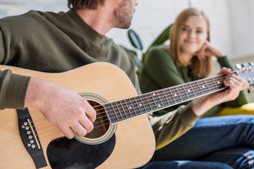 cropped shot of man playing on acoustic guitar to smiling girlfriend