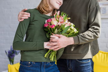 cropped image of man embracing smiling girlfriend with flowers