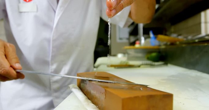 Male chef sharpening knife on a whetstone in kitchen 