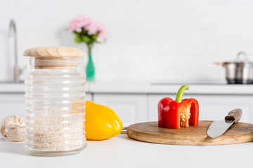 rice in glass jar and bell peppers on wooden board with knife