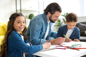 Obraz premium adorable child smiling at camera while drawing with father and brother at home