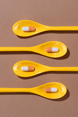 top view of pills in yellow plastic spoons on brown