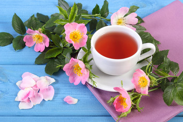 Fototapeta na wymiar Cup of hot tea and wild rose flower on blue boards