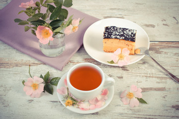 Vintage photo, Cup of tea with cheesecake and wild rose flower on old plank