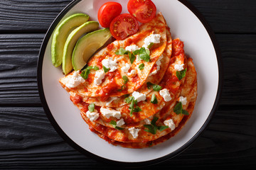 Mexican food: entomatadas with farm cheese, tomato sauce, greens and avocado close-up. horizontal top view