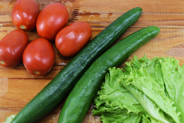 fresh juicy red tomatoes, cucumbers and lettuce on a wooden table