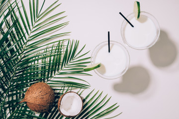 top view of organic coconuts, green palm leaves and coconut cocktails in glasses with drinking straws on white