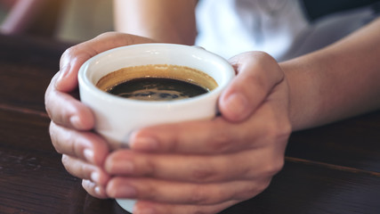 Closeup image of hands holding a cup of hot coffee on wooden table in cafe