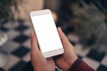 Mockup image of hands holding and using white mobile phone with blank screen in cafe