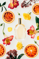 top view of bottle of aromatic perfume surrounded with flowers and blood orange slices on white