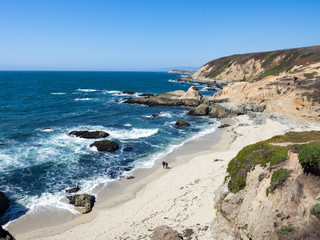 Barefoot hikers on beach below rocky cliffs and waves along shore in Bodea Head, Marin County, California, United States