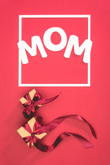top view of gift boxes with ribbons and word mom in frame on red surface, mothers day concept