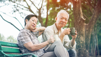 Asian senior couple relax drinking coffee in summer park, green nature