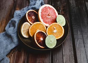 closeup view of halfs of orange, grapefruit, lime, blood orange and lemon in plate and kitchen towel on wooden table