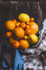 top view of oranges, tangerines, lemons, kumquats in plate and kitchen towels on wooden table