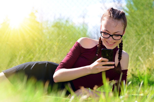 Caucasian teenager girl liyng in grass on garden and using a smart phone.