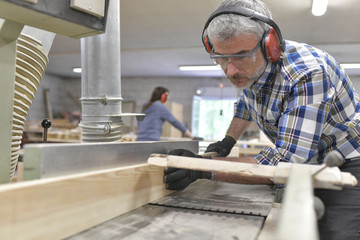 Wood worker cutting piece of wood with machine - obrazy, fototapety, plakaty