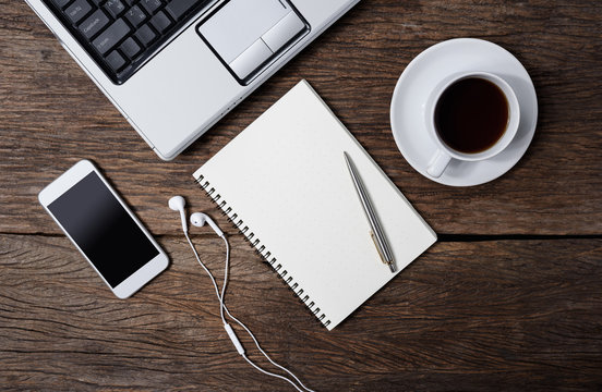 Office wooden desk with pen, notepad, coffee cup, smartphone and earphones. Top view