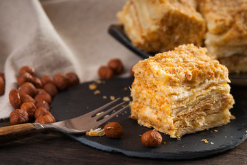 Slices of sweet classic layered cake Napoleon, fork and hazelnuts 