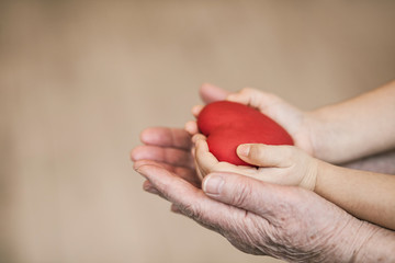 Red heart in child kid and grandmother hands on the light background