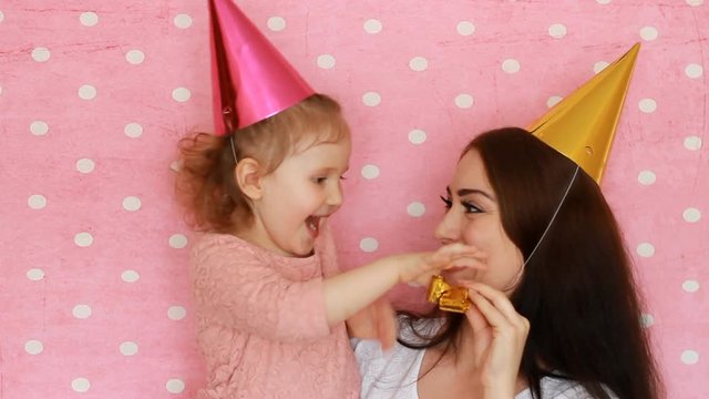 Woman and child blow horns, smiling and laughing. Mother and daughter blowing horn and having fun. Happy Birthday